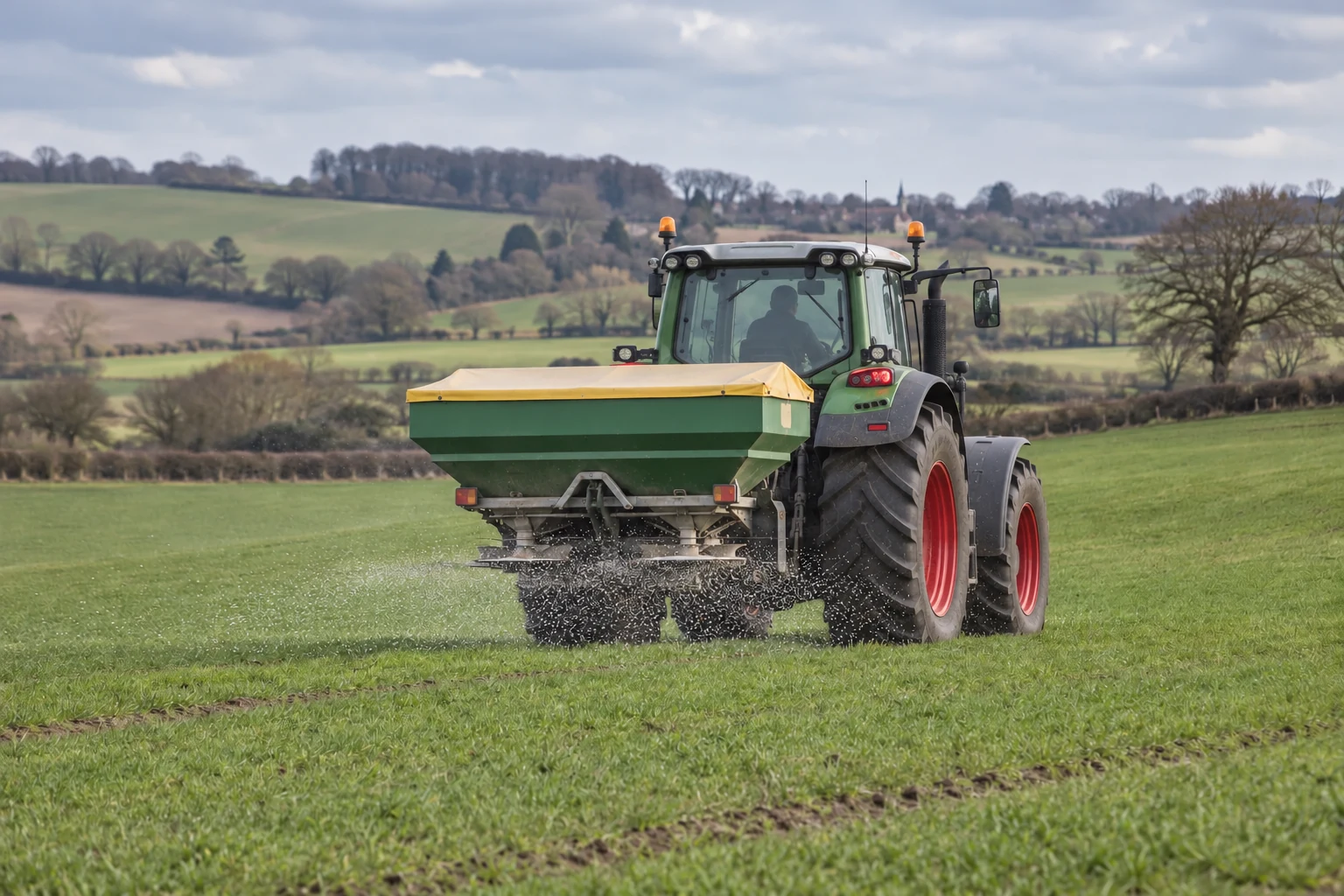 Illustrative marketing scene of a green tractor with red wheel rims applying fertiliser to a field